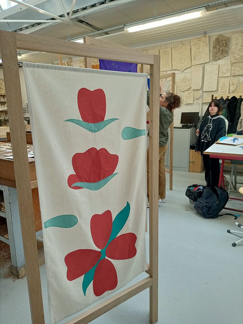 photo d'un étendoir crée lors du projet mené avec des élèves. en bois clair, le tissu est blanc avec des fleurs rouges et vertes