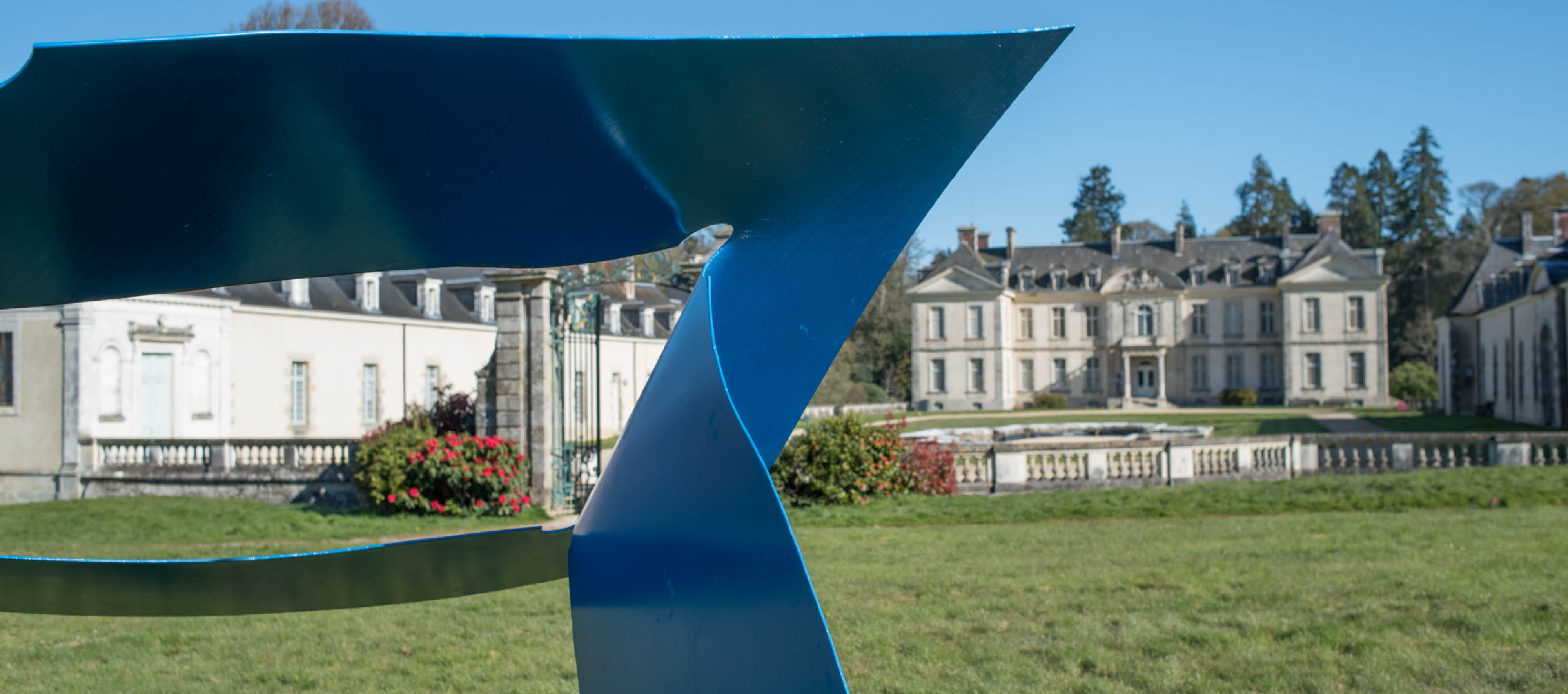 Photo du château à l'arrière-plan et d'une oeuvre formée d'un cadre en métal bleu au premier plan.