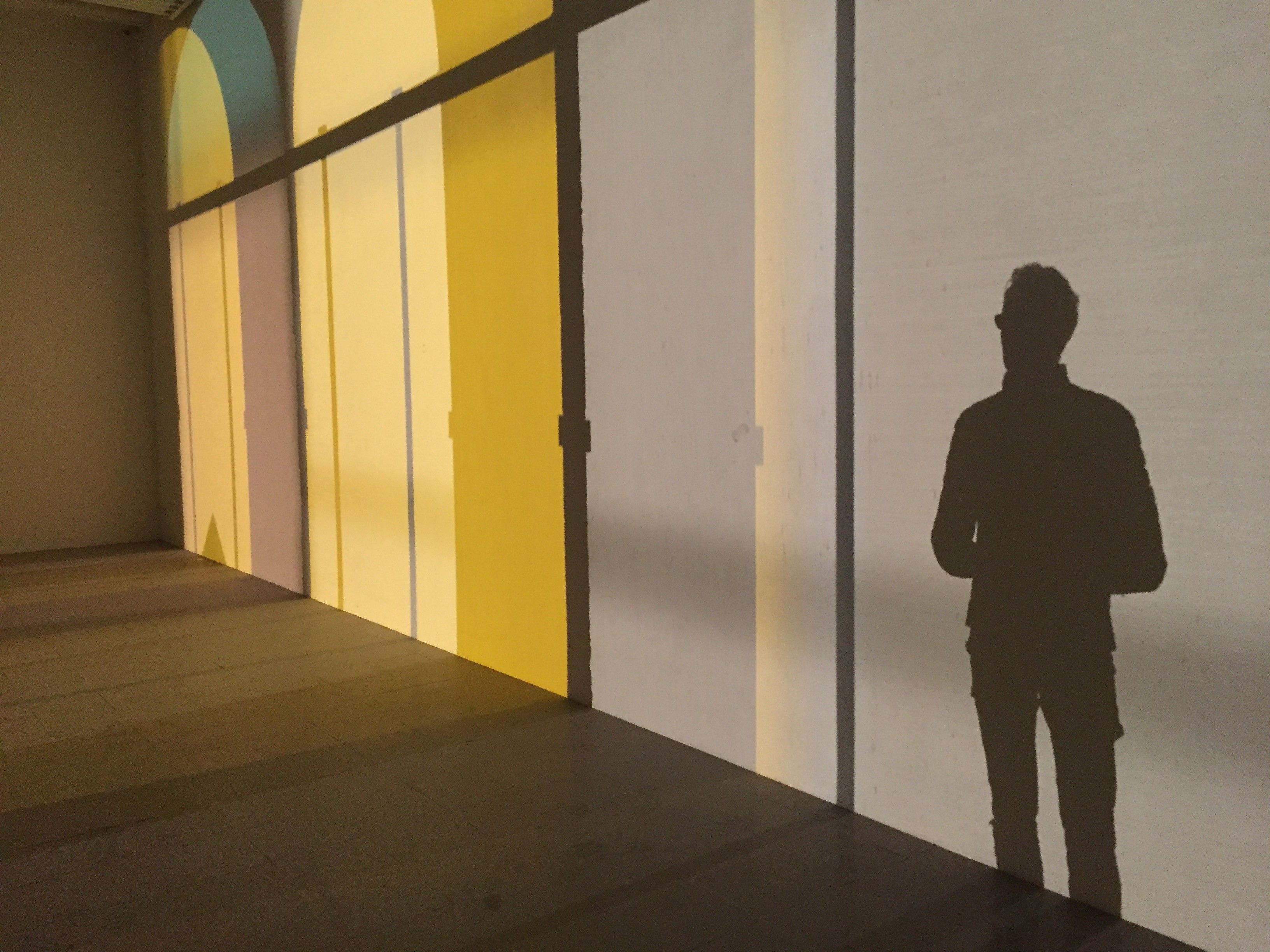 Vue d'une silhouette d'homme et de formes de fenêtres se détachant sur un mur grâce à un éclairage particulier.