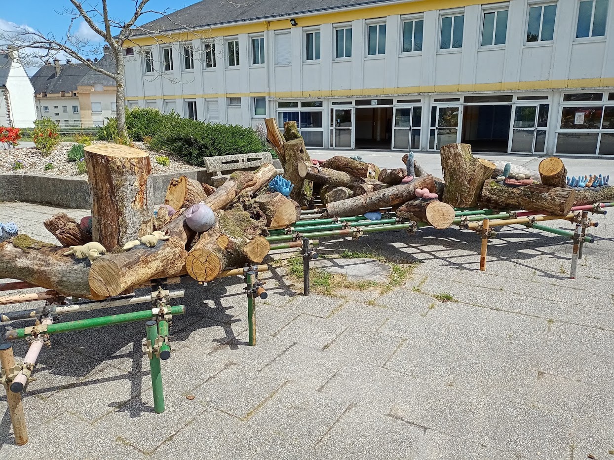 Morceaux de troncs d'arbres disposés sur un socle dans la cour d'un collège.