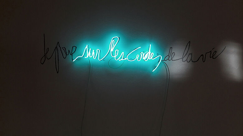 Photo d'une oeuvre de Françoise Réau : les mots "sur les cordes" en néon bleu plongés dans le noir.