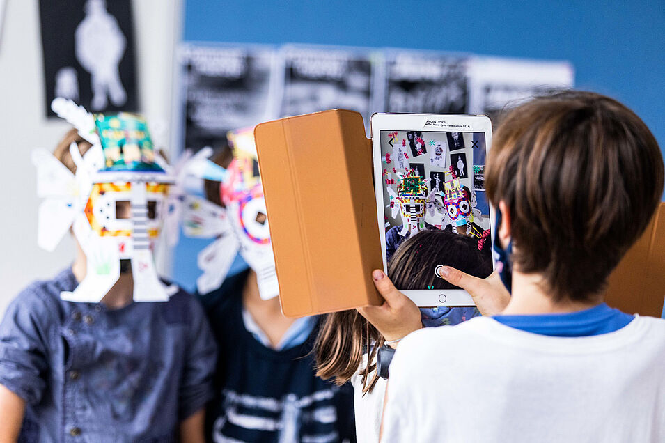 Photo d'un enfant prenant en photo avec une tablette deux autres enfants masqués.