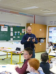 Homme intervenant devant des élèves de primaire, dans une salle de classe.