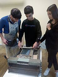 Une homme en atelier, un jeune homme et une jeune fille réalisent l'impression d'une gravure sur une presse.