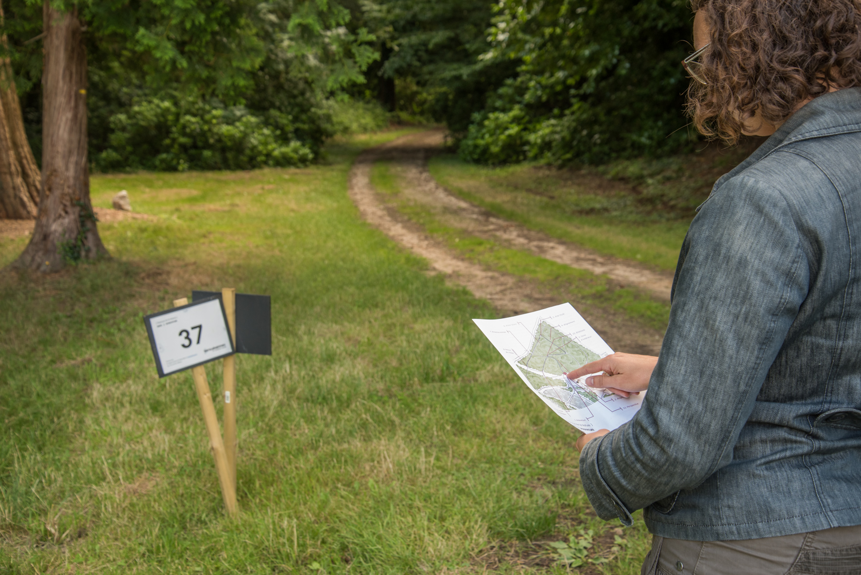 Personne avec un support papier à l'entrée de l'arboretum marqué par un panneau.